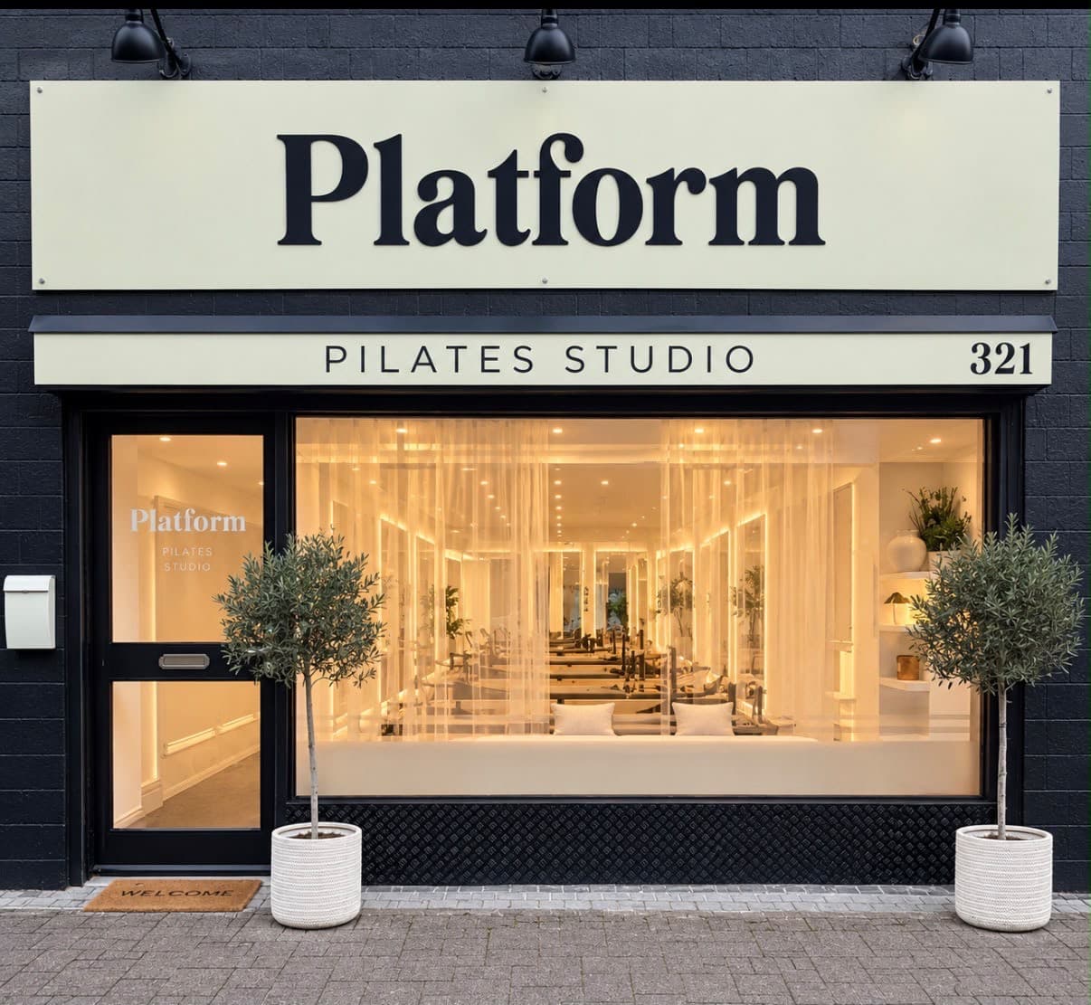 Platform Pilates Coleraine storefront, with a warmly lit studio behind the window and two potted trees outside