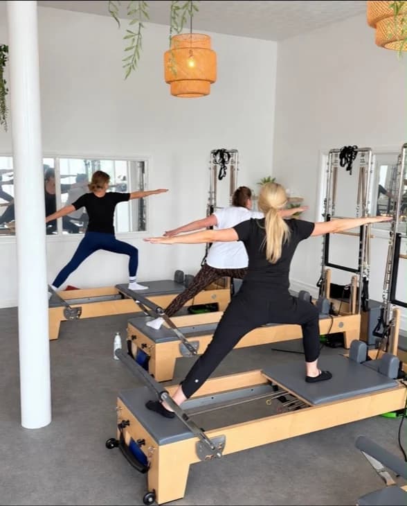 Clients holding a standing lunge with arms extended on their reformers in the Ebrington studio