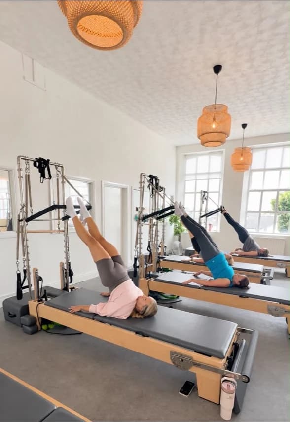 Three clients exercising with their feet in straps on Tower equipment in the Ebrington studio